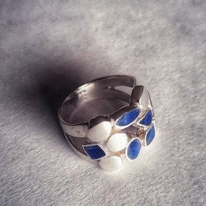 May include: A silver ring with blue and white stones set in a geometric pattern.