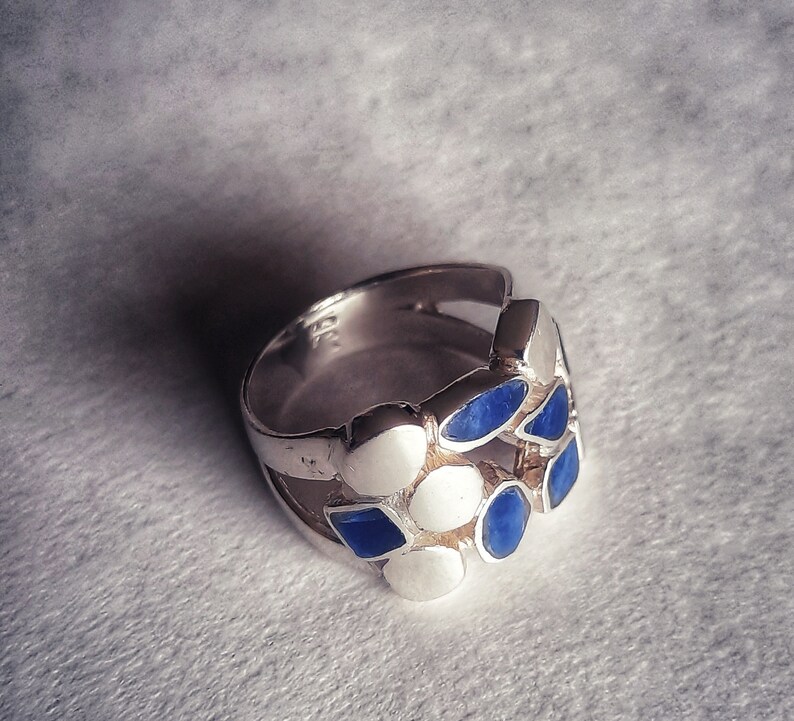 May include: A silver ring with blue and white stones set in a geometric pattern.