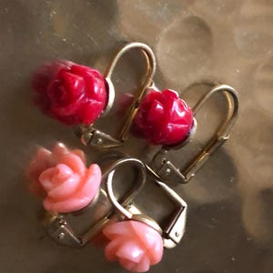 Può includere: Un paio di orecchini a clip dorati con pietre a forma di rosa rossa e rosa.