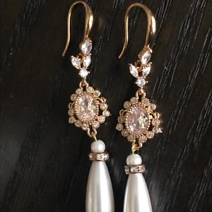 May include: Gold dangle earrings with a pearlescent teardrop charm and a cluster of clear rhinestones.