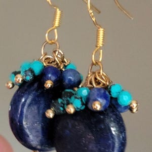 May include: Gold earrings with a cluster of blue and turquoise gemstone beads. The earrings feature a large, oval-shaped blue gemstone.