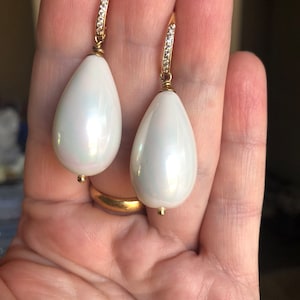 May include: A pair of white teardrop-shaped pearl earrings with gold settings and a row of clear cubic zirconia stones on the dangle.