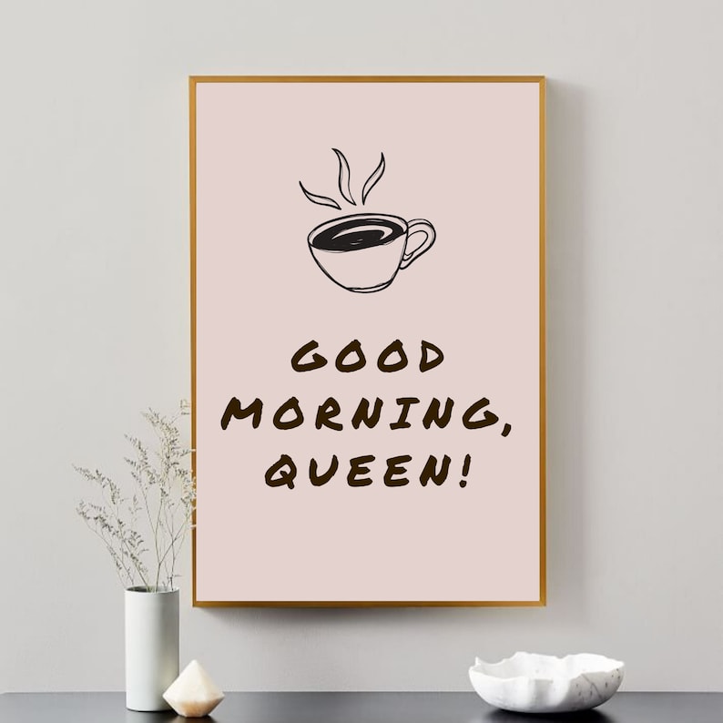May include: A pink and gold framed print with a black and white illustration of a coffee cup with steam rising from it. The text "GOOD MORNING, QUEEN!" is written in black below the illustration.