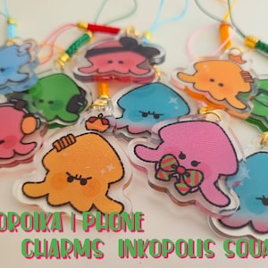 May include: A collection of colorful, cartoon-style phone charms featuring various squid-like characters. The charms are in shades of blue, green, pink, and orange, with decorative accents and attached lanyards. Text on the image reads "COROIKA I PHONE CHARMS INKOPOLIS SQUARE."