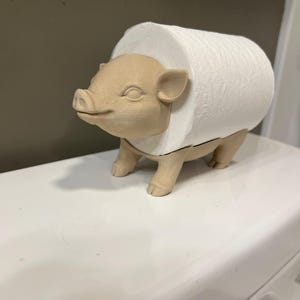 May include: A brown ceramic pig toilet paper holder with a white roll of toilet paper inside.