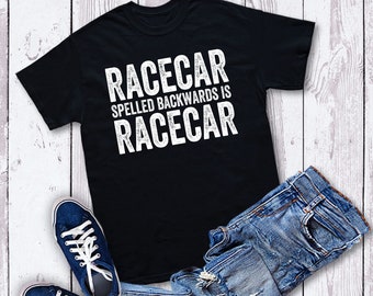 Op de afbeelding: Zwart T-shirt met witte tekst die "Racecar spelled backwards is racecar" zegt. Het shirt ligt op een wit houten oppervlak met een blauwe spijkerbroek en blauwe sneakers.