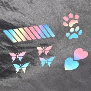 May include: A black fabric background with colorful iron-on patches. The patches include a rainbow stripe, two butterflies, a paw print, and two hearts.