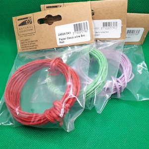 Può includere: Tre bobine di filo di carta per l'artigianato. Le bobine sono rosse, verdi e viola. La bobina rossa è etichettata "Paper Deco wire 6m Red". La bobina verde è etichettata "deco wire 5m green".