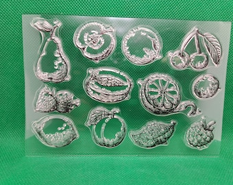 Puede incluir: Una hoja transparente de sellos con diferentes frutas y verduras. Los sellos están diseñados para manualidades y scrapbooking. Los diseños incluyen una pera, un limón, una lima, una cereza, una fresa, una frambuesa, una ciruela y una sandía.