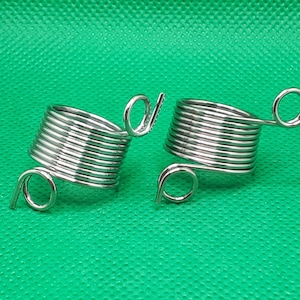 Op de afbeelding: Twee zilveren metalen draadhouders met een lus aan de zijkant. De draadhouders zijn gewikkeld en zijn bedoeld om aan een vinger te worden gedragen.