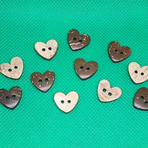 Könnte beinhalten: Zehn herzförmige Knöpfe aus Kokosnussschale in Braun und Naturfarben. Die Knöpfe haben jeweils zwei Löcher.