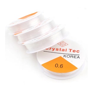 Könnte beinhalten: Drei Spulen mit klarem elastischem Faden zum Schmuckmachen. Die Spulen sind mit "Crystal Tec Korea 0.6" beschriftet.
