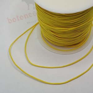 May include: A spool of bright yellow elastic cord. The cord is wound tightly around the spool and is ready to be used for crafting projects.