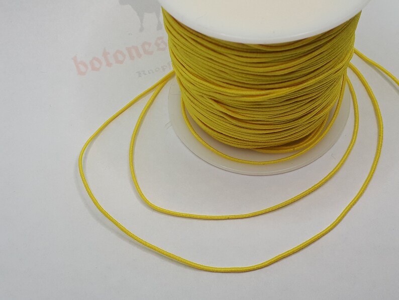 May include: A spool of bright yellow elastic cord. The cord is wound tightly around the spool and is ready to be used for crafting projects.