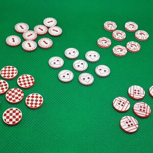 Könnte beinhalten: Sortiment weißer Knöpfe mit roten Designs. Einige Knöpfe haben ein kariertes Muster, andere haben Herzen und wieder andere haben ein Blumenmuster.