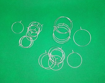 May include: A collection of silver hoop earrings on a green background. The earrings are arranged in three groups, with some stacked on top of each other.