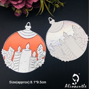 Könnte beinhalten: Zwei metallene Weihnachtsbaumschmuck-Stanzformen, eine mit rotem Hintergrund und die andere mit silbernem Hintergrund. Beide Ornamente zeigen ein Design aus drei Kerzen mit Stechpalmenblättern. Die Stanzformen sind etwa 8,1 cm x 9,5 cm groß.