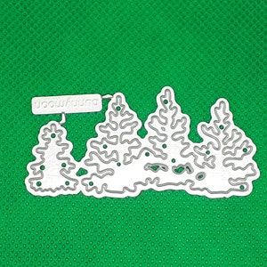 Könnte beinhalten: Eine weiße Metallstanzform mit einer Reihe von fünf stilisierten Bäumen mit dem Wort "woodland" auf einem weißen Banner über den Bäumen.