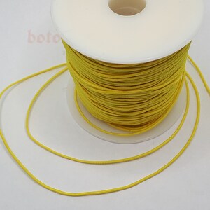 May include: A spool of bright yellow elastic cord. The cord is wound around a white plastic spool.