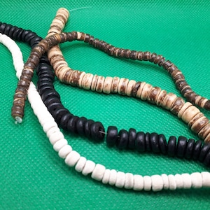 May include: Three strands of wooden beads, one white, one black, and one brown. The beads are all round and have a slightly irregular shape.