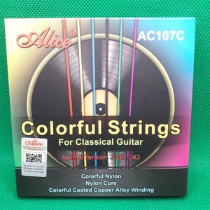 May include: A pack of Alice AC107C Colorful Strings for Classical Guitar. The packaging features a colourful image of guitar strings against a black background. The text on the pack reads "Normal Tension 028-1043", "Colorful Nylon", "Nylon Core", and "Colorful Coated Copper Alloy Winding".