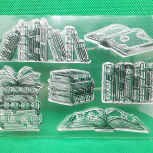 Könnte beinhalten: Klare Stempel-Set mit Buchillustrationen. Das Set enthält Stapel von Büchern, offene Bücher und Bücher auf einem Regal, alles im detaillierten Strichstil. Ideal für Bastel- und Scrapbooking-Projekte.