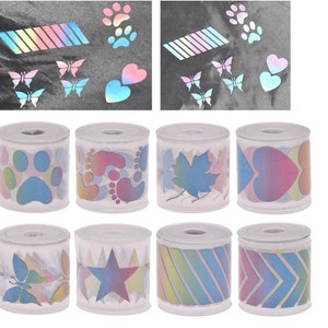 May include: Eight rolls of iridescent holographic washi tape with various designs, including paw prints, hearts, butterflies, stars, and stripes. The tape is on white spools.