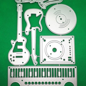 May include: Metal die cuts for crafting, featuring a saxophone, guitar, record player, and a keyboard. The dies are silver and have a detailed design.