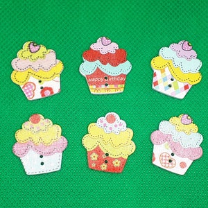 Può includere: Sei bottoni di legno a forma di cupcake colorati con vari disegni, tra cui un cupcake rosa e giallo con la scritta "Happy Birthday" sopra.