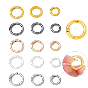 Könnte beinhalten: Eine Auswahl an runden Federring-Verschlüssen in verschiedenen Größen und Ausführungen. Die Verschlüsse sind in Gold, Gunmetal, Roségold und Silber dargestellt. Ein Verschluss wird in einer Hand gehalten, um sein offenes Design zu zeigen. Diese Verschlüsse sind ideal für die Schmuckherstellung.