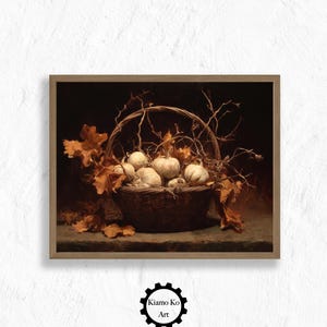 May include: A framed print featuring a still life of a basket filled with white pumpkins, surrounded by dried leaves and twigs. The artwork has a warm, autumnal color palette with a dark background. The frame is a light brown color. The print is from Kiamo Ko Art.