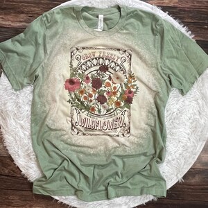 K&ouml;nnte beinhalten: Gr&uuml;nes T-Shirt mit einem Vintage-Grafikdruck von Blumen und dem Text "Grow Freely Wildflower".