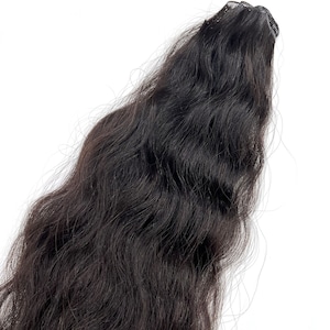 Puede incluir: Una extensión de cabello oscuro y ondulado sobre un fondo blanco. El cabello es de color negro intenso y parece largo y fluido. La extensión tiene una pinza en la parte superior para una fácil fijación.