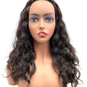 May include: A dark brown human hair wig with loose waves. The wig is worn on a mannequin head and has a black elastic headband.