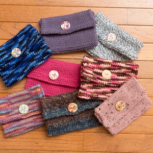May include: Eight knitted pouches with different patterns and colors, each with a button closure. The pouches are arranged in a circle on a wooden surface.