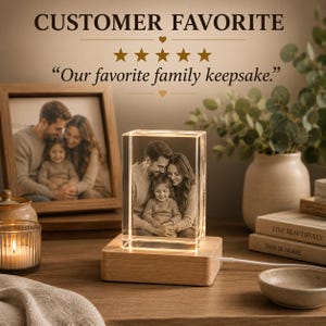 May include: A rectangular glass block featuring a laser-etched 3D image of a family of three, illuminated by a light-colored wooden base. The text CUSTOMER FAVORITE, five stars, and the quote Our favorite family keepsake are displayed above.