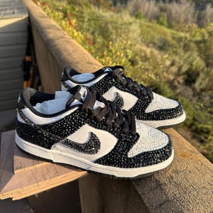 K&ouml;nnte beinhalten: Paar schwarz-wei&szlig;e Sneaker mit einem Schmuckdesign. Die Schuhe haben einen wei&szlig;en Nike-Swoosh, schwarze Schn&uuml;rsenkel und eine wei&szlig;e Sohle. Das Obermaterial ist mit schwarzen und wei&szlig;en Verzierungen bedeckt.