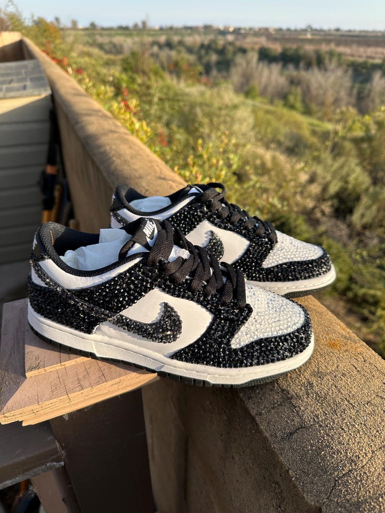 K&ouml;nnte beinhalten: Paar schwarz-wei&szlig;e Sneaker mit einem Schmuckdesign. Die Schuhe haben einen wei&szlig;en Nike-Swoosh, schwarze Schn&uuml;rsenkel und eine wei&szlig;e Sohle. Das Obermaterial ist mit schwarzen und wei&szlig;en Verzierungen bedeckt.