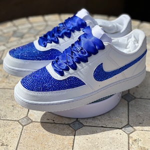 May include: White leather sneakers with a blue satin ribbon tied around the laces. The sneakers are covered in blue rhinestones.