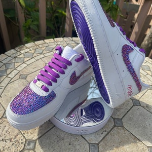 May include: White leather sneakers with purple laces and a purple trim. The sneakers are covered in iridescent rhinestones and have the word "MRS" written on the side.