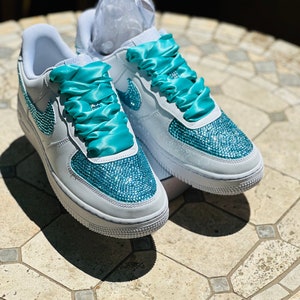 May include: White sneakers with turquoise blue ribbon laces and a turquoise blue rhinestone design.
