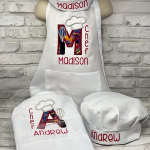 May include: Two white chef hats with red embroidery. One hat says "Chef Andrew" with a colorful letter A and a chef hat graphic. The other hat says "Andrew".