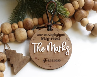 May include: A round wooden Christmas ornament with the text "Our 1st Christmas Married The Marks est. 8.23.2023" in white lettering.