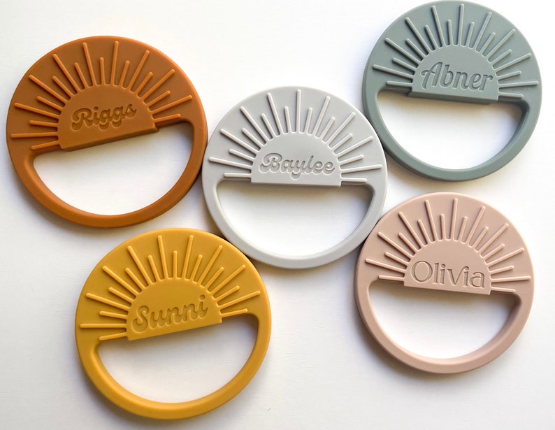May include: Five silicone teething rings in different colors with a sunburst design and personalized names: Riggs, Baylee, Abner, Olivia, and Sunni.