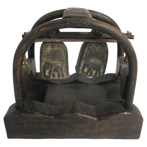 May include: A wooden musical instrument with two bells that are shaped like elephant feet. The bells are suspended from a wooden frame and are attached to a wooden base.