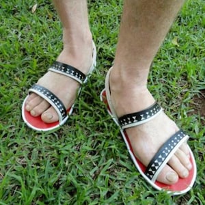 以下が含まれることがあります： 赤色の縁取りが付いた黒と白の色のサンダル。サンダルには、ストラップに幾何学模様が施されています。