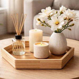 May include: A wooden hexagonal tray displays a reed diffuser, two lit candles, and a small white vase with white flowers. The items are on a round wooden coffee table, creating a cosy, inviting atmosphere.