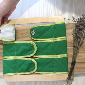 Puede incluir: Un marco de madera con tiras de tela verde con ribetes amarillos y cierres de bot&oacute;n. Las tiras de tela est&aacute;n cosidas con un patr&oacute;n de diamante. El marco est&aacute; sobre una superficie de madera con un ramo de lavanda seca.