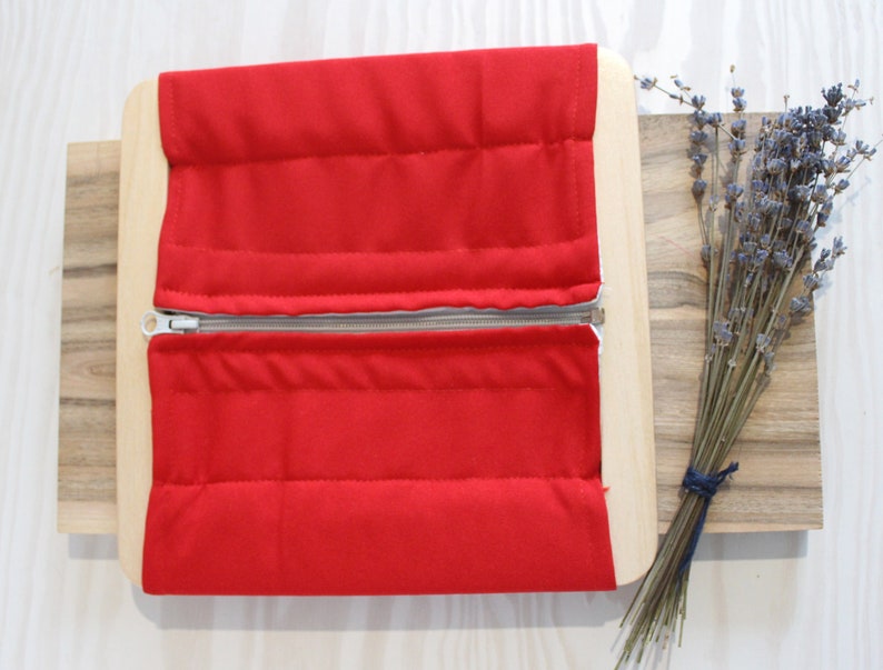 Puede incluir: Una tabla de cremallera roja con una cremallera que recorre el centro. La tabla est&aacute; hecha de madera y tiene una superficie de tela acolchada.