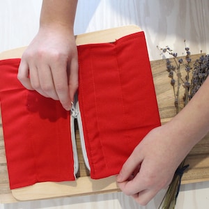 Puede incluir: Una actividad de cremallera de tela roja para ni&ntilde;os. La cremallera est&aacute; parcialmente abierta y la tela est&aacute; sobre una tabla de madera.